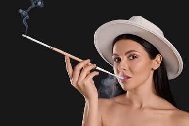 Woman using long cigarette holder for smoking on black background