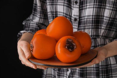Photo of Woman holding delicious ripe juicy persimmons on black background, closeup