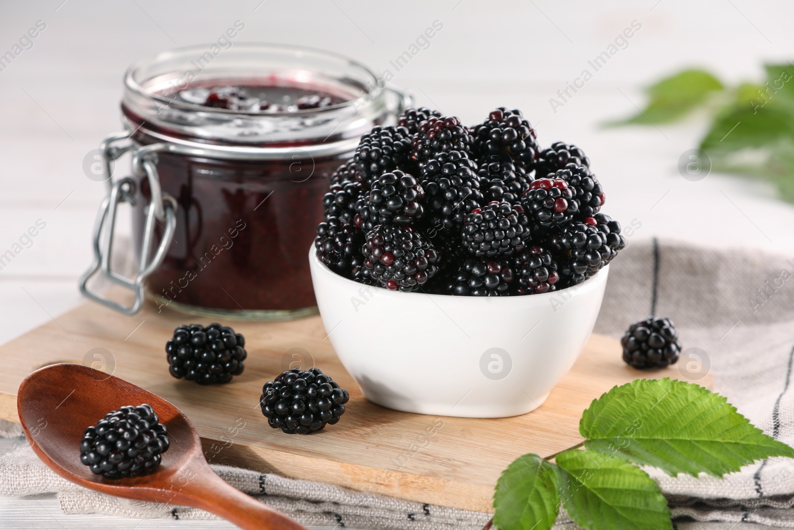 Photo of Fresh ripe blackberries, tasty jam and leaves on wooden board, closeup