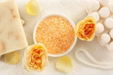 Bowl with sea salt, soap bar and beautiful roses on white towel, flat lay