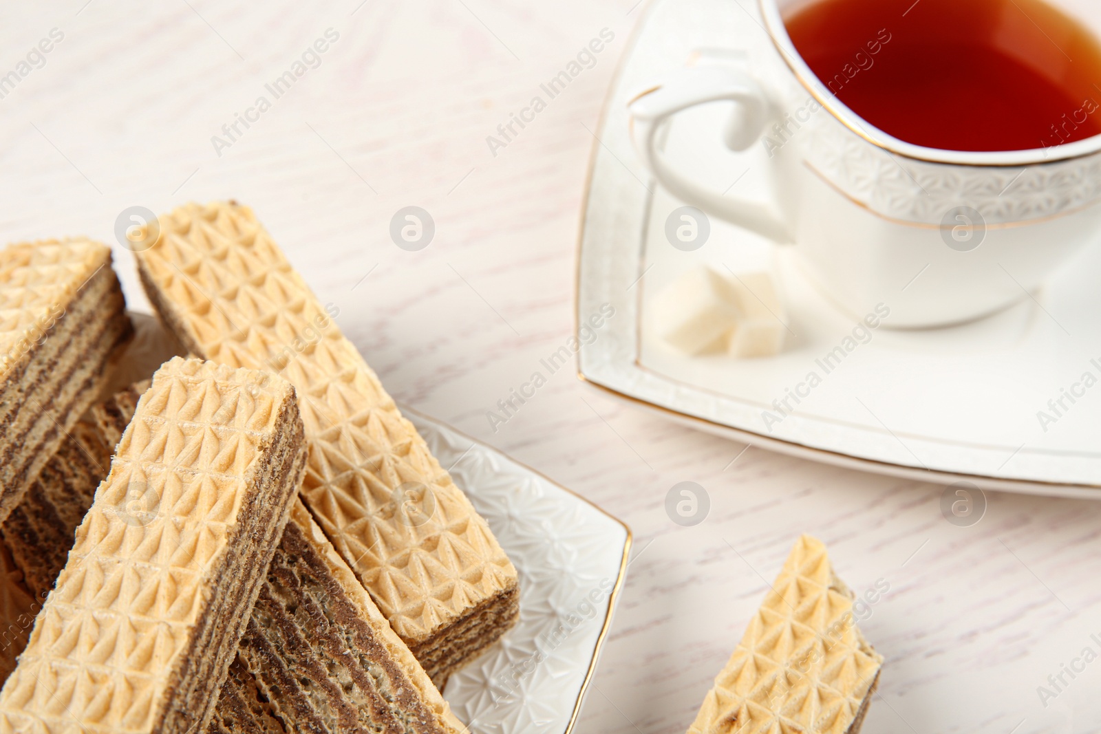 Photo of Plate of delicious wafers with cup of tea on white wooden background, closeup