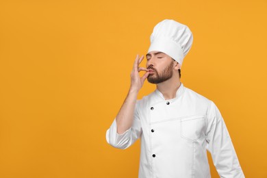 Mature chef showing delicious gesture on orange background, space for text