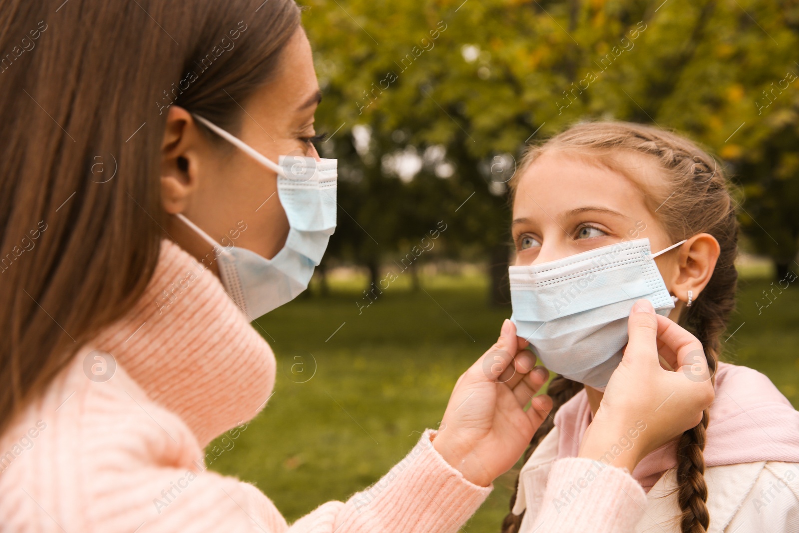 Photo of Mother putting mask onto face of little daughter in park during coronavirus pandemic