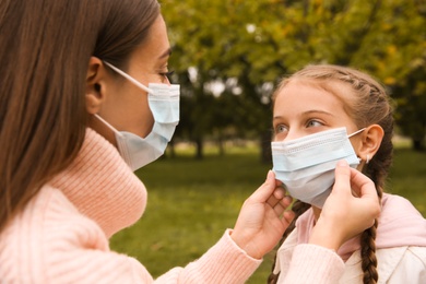 Mother putting mask onto face of little daughter in park during coronavirus pandemic