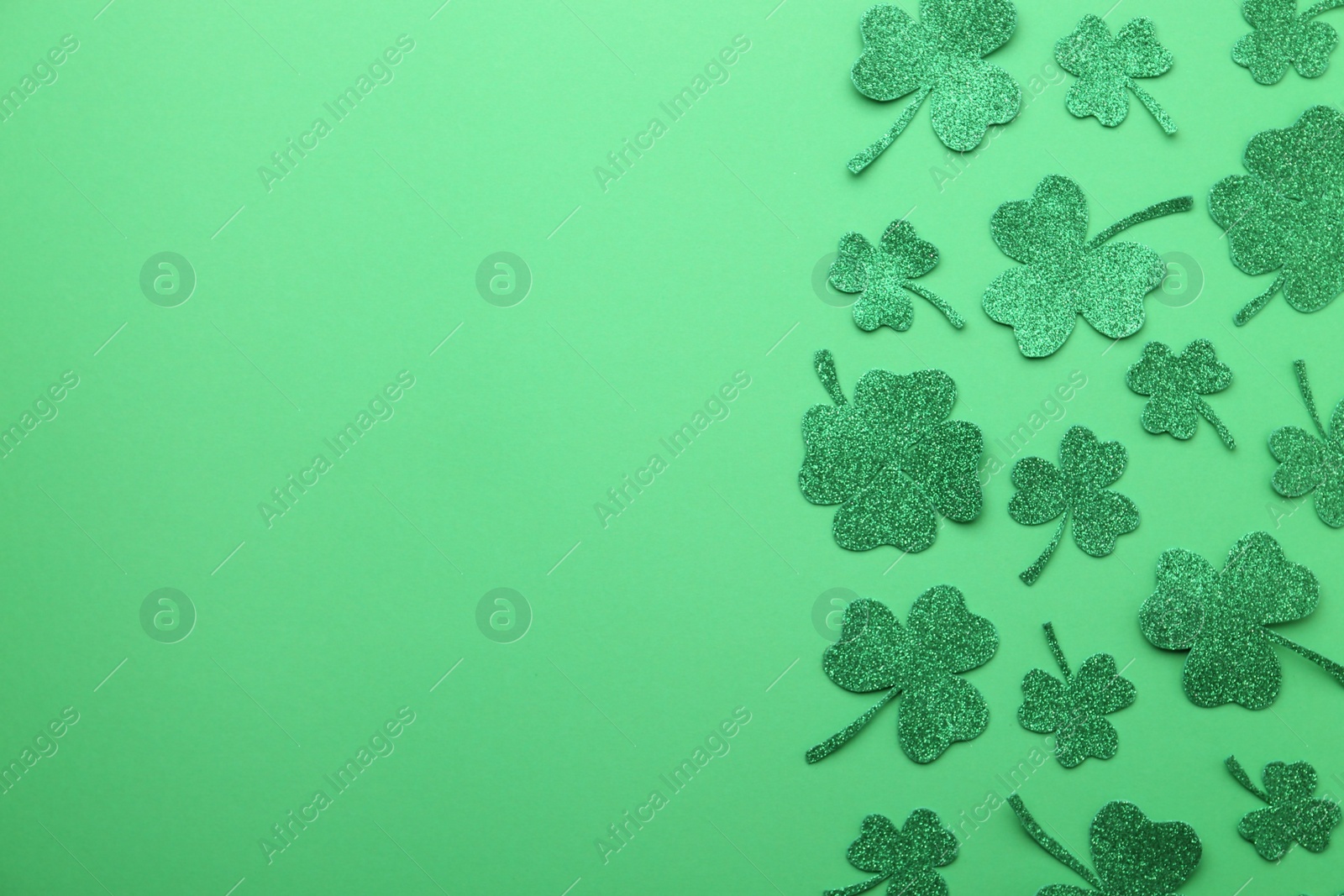 Photo of St. Patrick's day. Shiny decorative clover leaves on green background, flat lay. Space for text