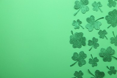 St. Patrick's day. Shiny decorative clover leaves on green background, flat lay. Space for text