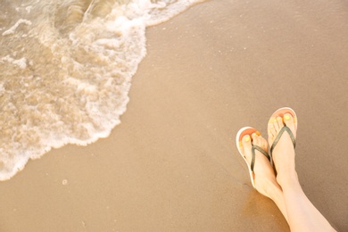 Photo of Closeup of woman with stylish flip flops on sand near sea, space for text. Beach accessories