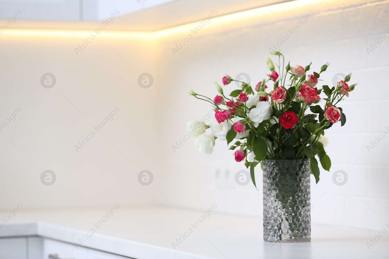 Photo of Vase with beautiful flowers on white countertop in kitchen, space for text