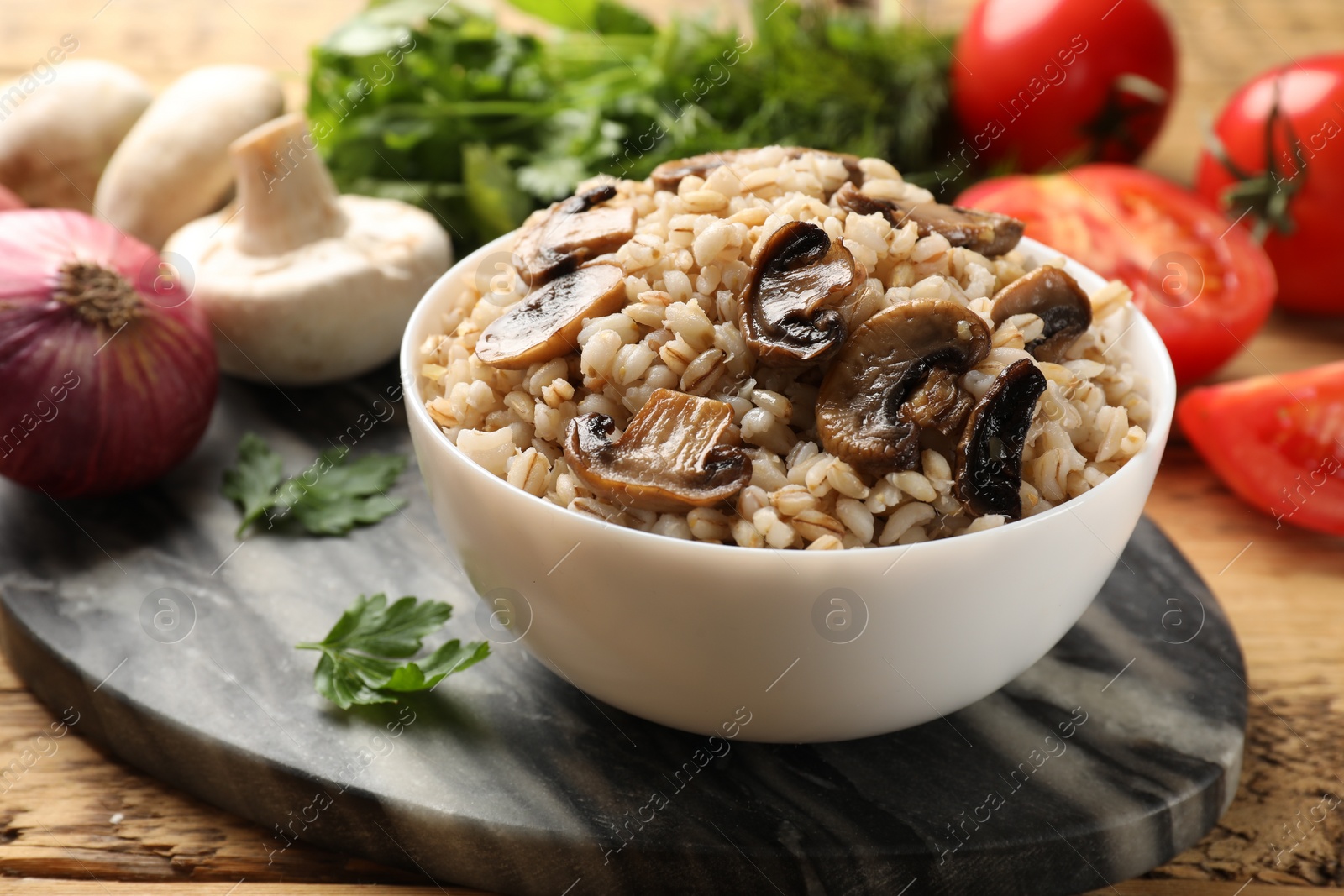 Photo of Delicious pearl barley with mushrooms in bowl served on wooden table, closeup