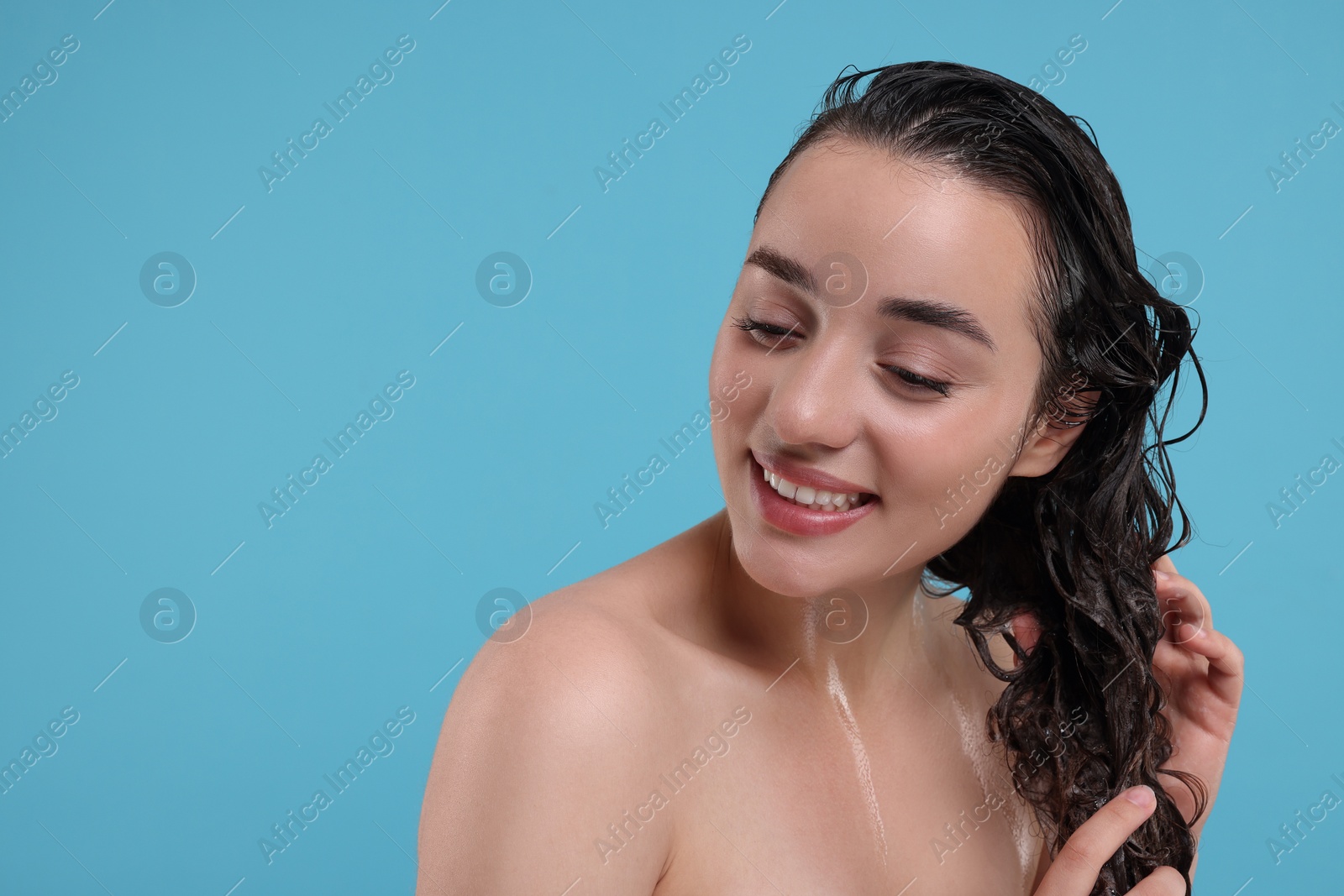 Photo of Beautiful happy woman washing hair on light blue background. Space for text