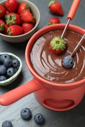 Dipping fresh berries in fondue pot with melted chocolate at grey table, above view