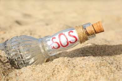 Photo of Glass bottle with SOS message on sand, closeup