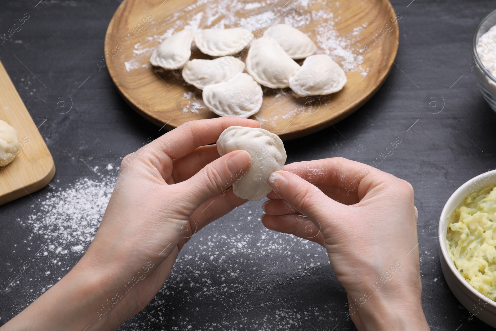 Photo of Woman making dumplings (varenyky) at black table, closeup