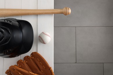 Photo of Baseball bat, batting helmet, leather glove and ball on white wooden bench indoors, top view. Space for text