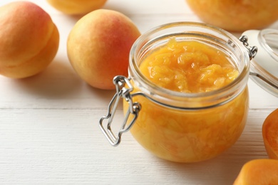 Photo of Jar of apricot jam and fresh fruits on white wooden table, closeup