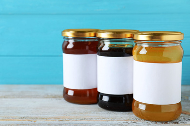 Jars of organic honey with blank labels on wooden table against light blue background. Space for text