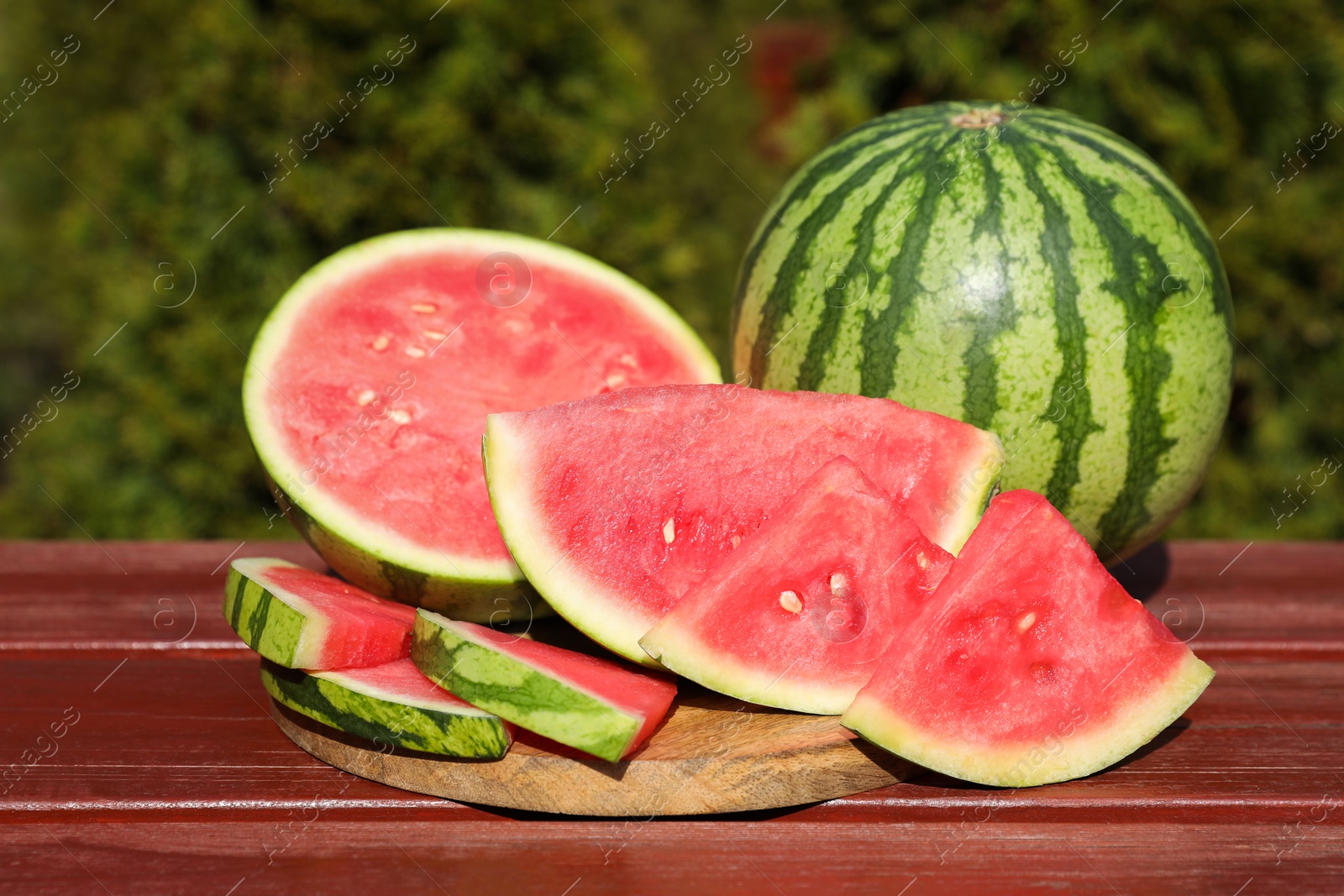 Photo of Delicious cut and whole ripe watermelons on wooden table outdoors