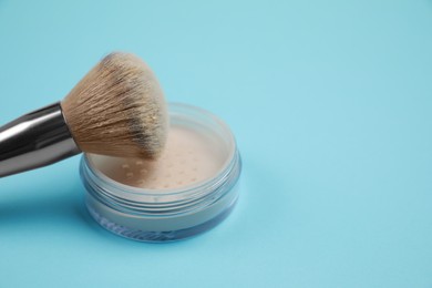 Loose face powder and brush on light blue background, space for text