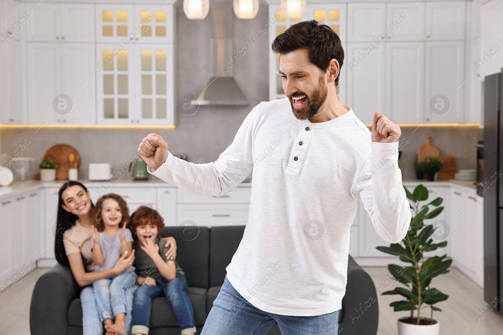 Photo of Happy family having fun at home. Father dancing while his relatives resting on sofa