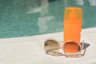 Photo of Stylish sunglasses and sunscreen near outdoor swimming pool on sunny day, space for text. Beach accessories