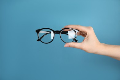 Photo of Woman holding glasses on blue background, closeup. Ophthalmologist prescription