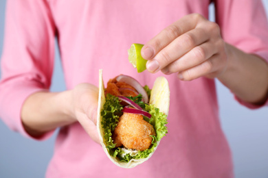 Photo of Woman squeezing lime on fish taco against grey background, closeup