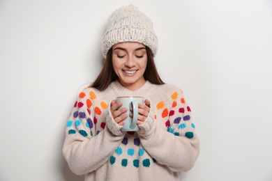 Beautiful young woman in warm sweater with cup of hot drink on white background