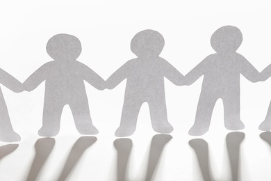 Photo of Paper people holding hands on light background. Unity concept