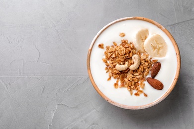 Photo of Bowl with yogurt, banana and granola on gray background, top view