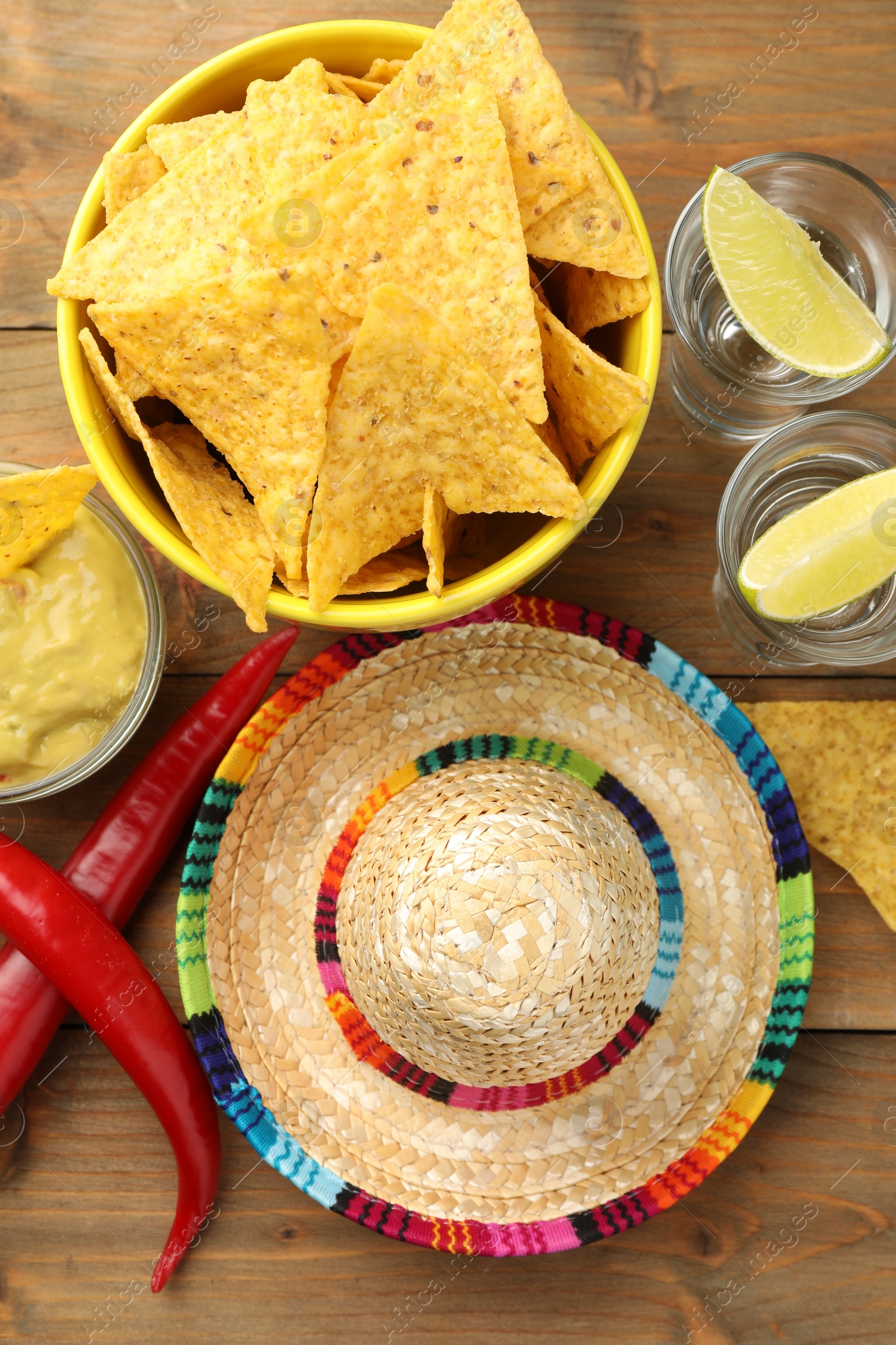 Photo of Mexican sombrero hat, tequila, chili peppers, nachos chips and guacamole on wooden table, flat lay