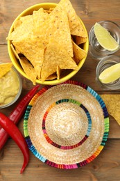 Mexican sombrero hat, tequila, chili peppers, nachos chips and guacamole on wooden table, flat lay
