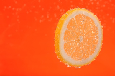 Photo of Slice of lemon in sparkling water on orange background, space for text. Citrus soda