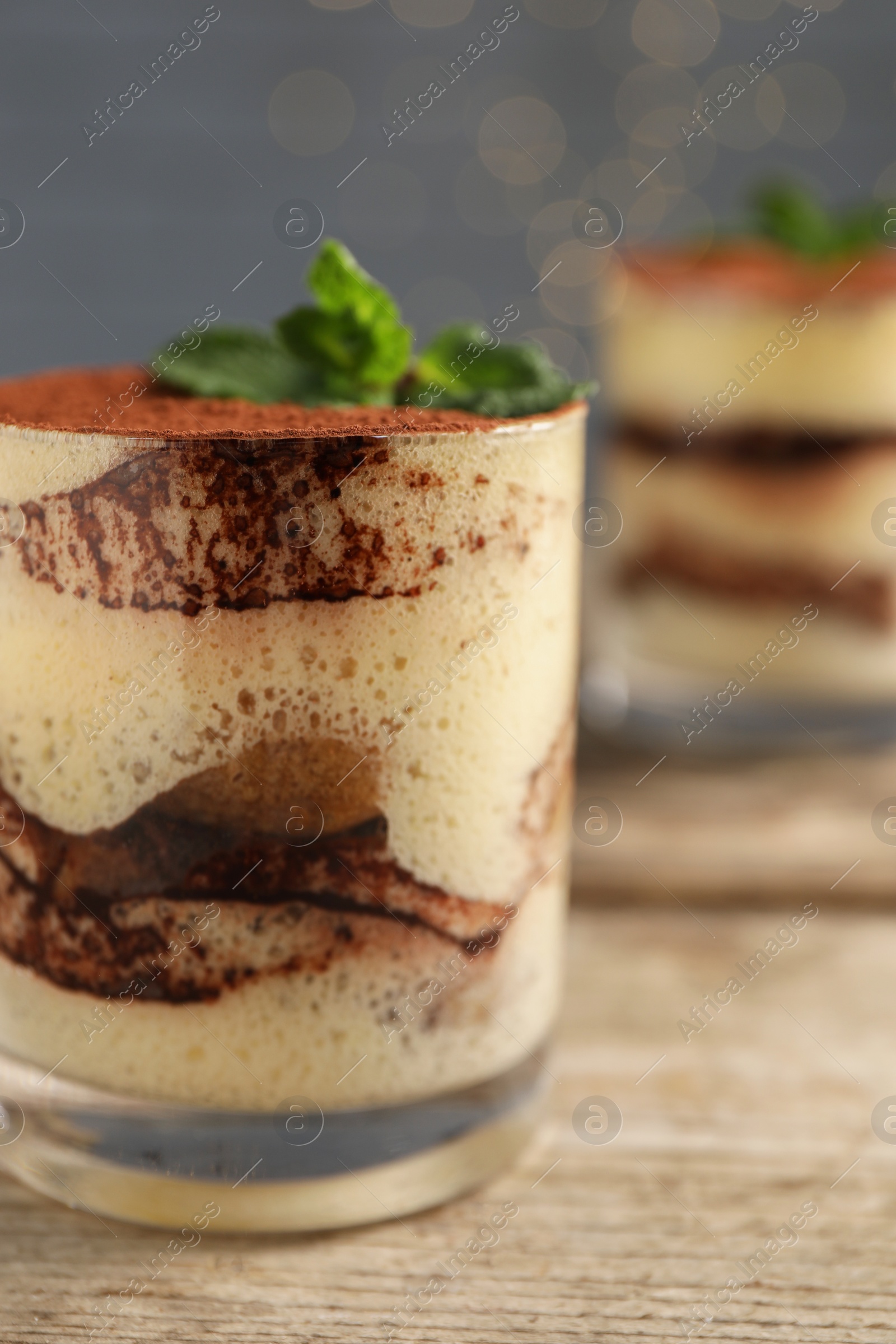 Photo of Tasty tiramisu and mint in glass on wooden table, closeup