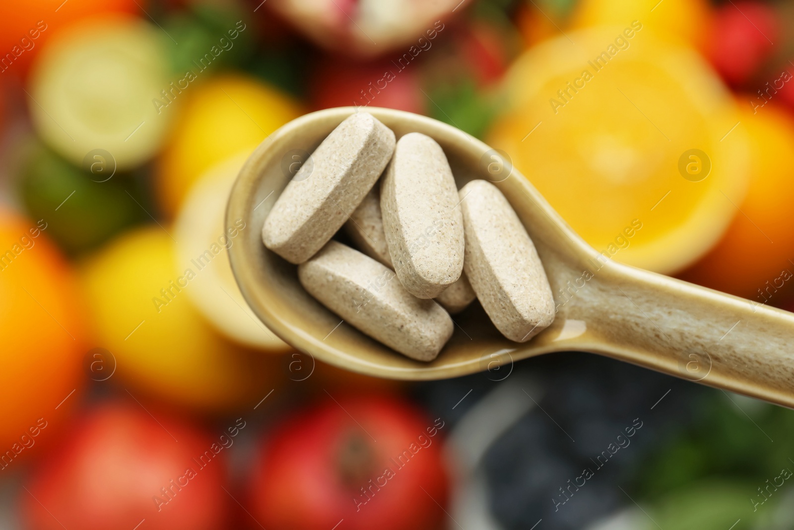 Photo of Vitamin pills in spoon over fresh fruits, top view