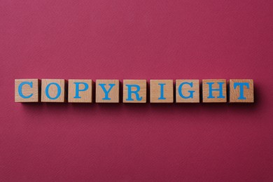 Photo of Wooden cubes with word Copyright on dark pink background, flat lay. Plagiarism concept