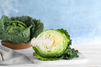 Photo of Half of fresh green savoy cabbage on white wooden table against light blue background