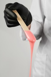 Photo of Woman in gloves holding spatula with hot depilatory wax, closeup