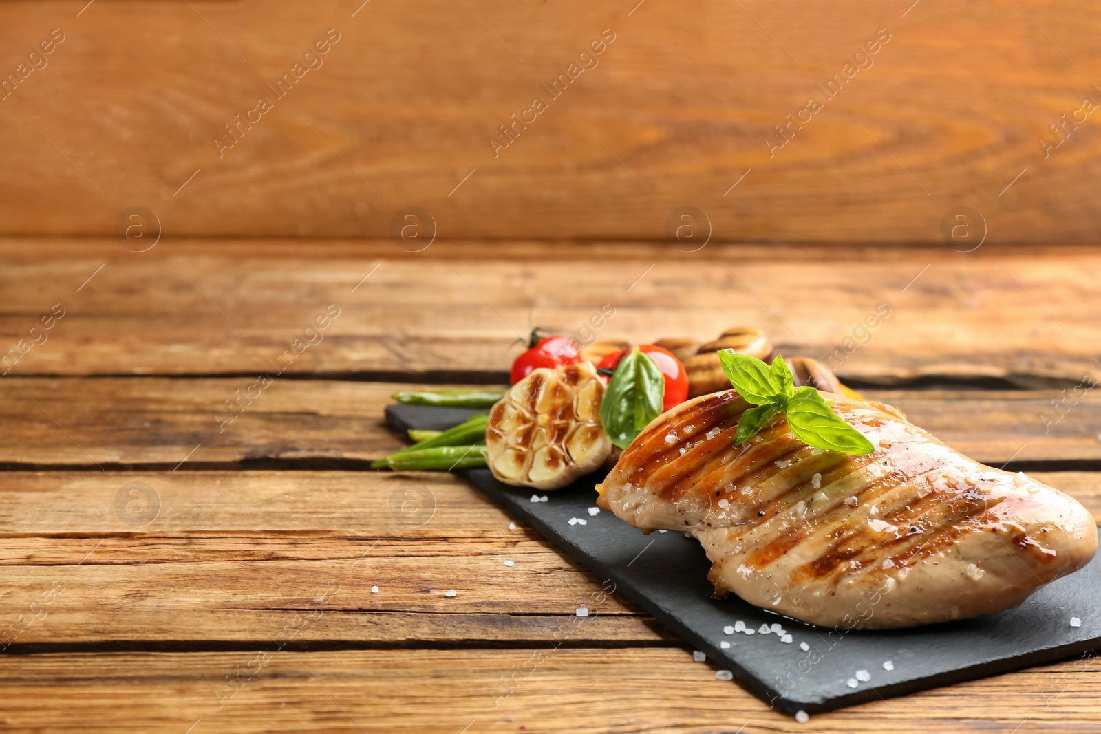 Photo of Tasty grilled chicken fillet with green basil on wooden table. Space for text