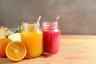 Mason jars with different juices and fresh fruits on wooden table against color background. Space for text