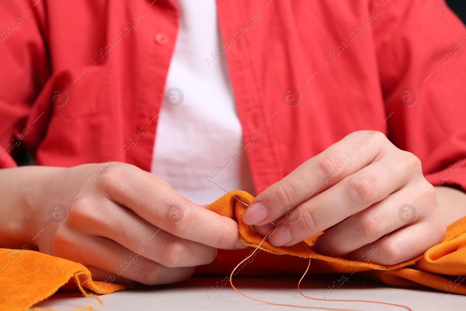Photo of Woman sewing cloth with needle at table, closeup