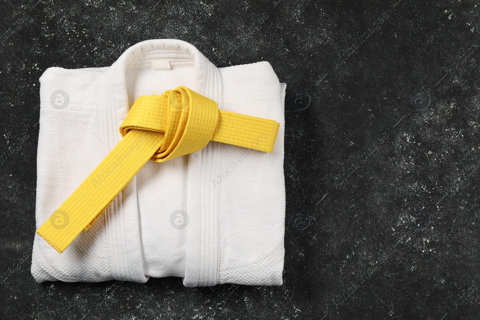 Photo of Yellow karate belt and white kimono on gray textured background, top view. Space for text