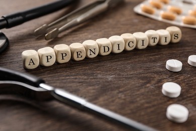 Photo of Word Appendicitis made of cubes, pills and medical supplies on wooden table, closeup