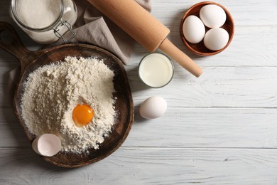 Photo of Pile of flour with yolk and other ingredients for dough on white wooden table, flat lay. Space for text