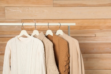 Photo of Collection of warm sweaters hanging on rack against wooden background