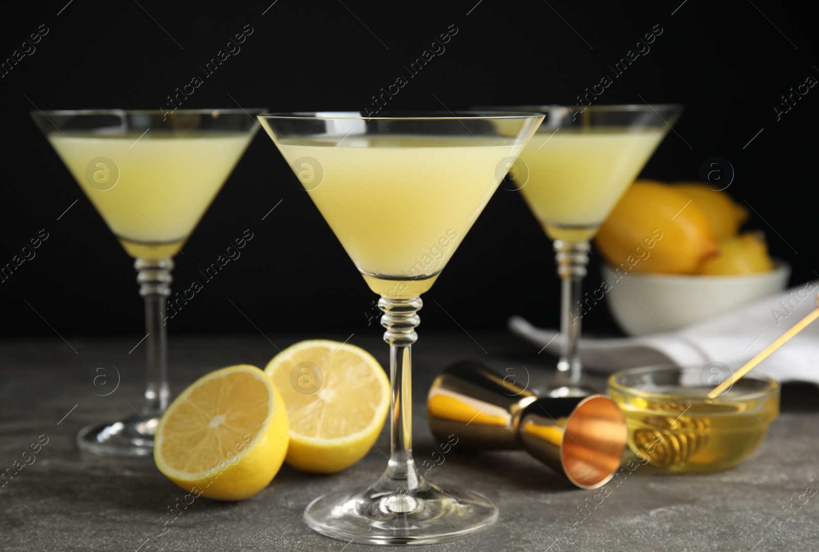 Photo of Delicious bee's knees cocktails and ingredients on grey table against black background