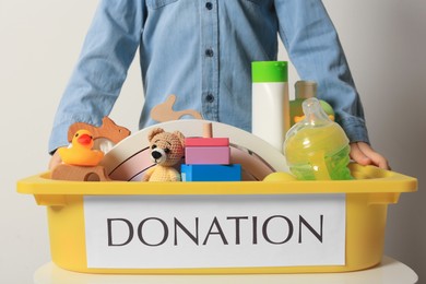 Photo of Little boy holding donation box with goods and toys against light background, closeup