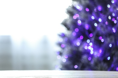 Photo of Blurred view of beautiful Christmas tree with purple lights near window indoors, focus on wooden table. Space for text