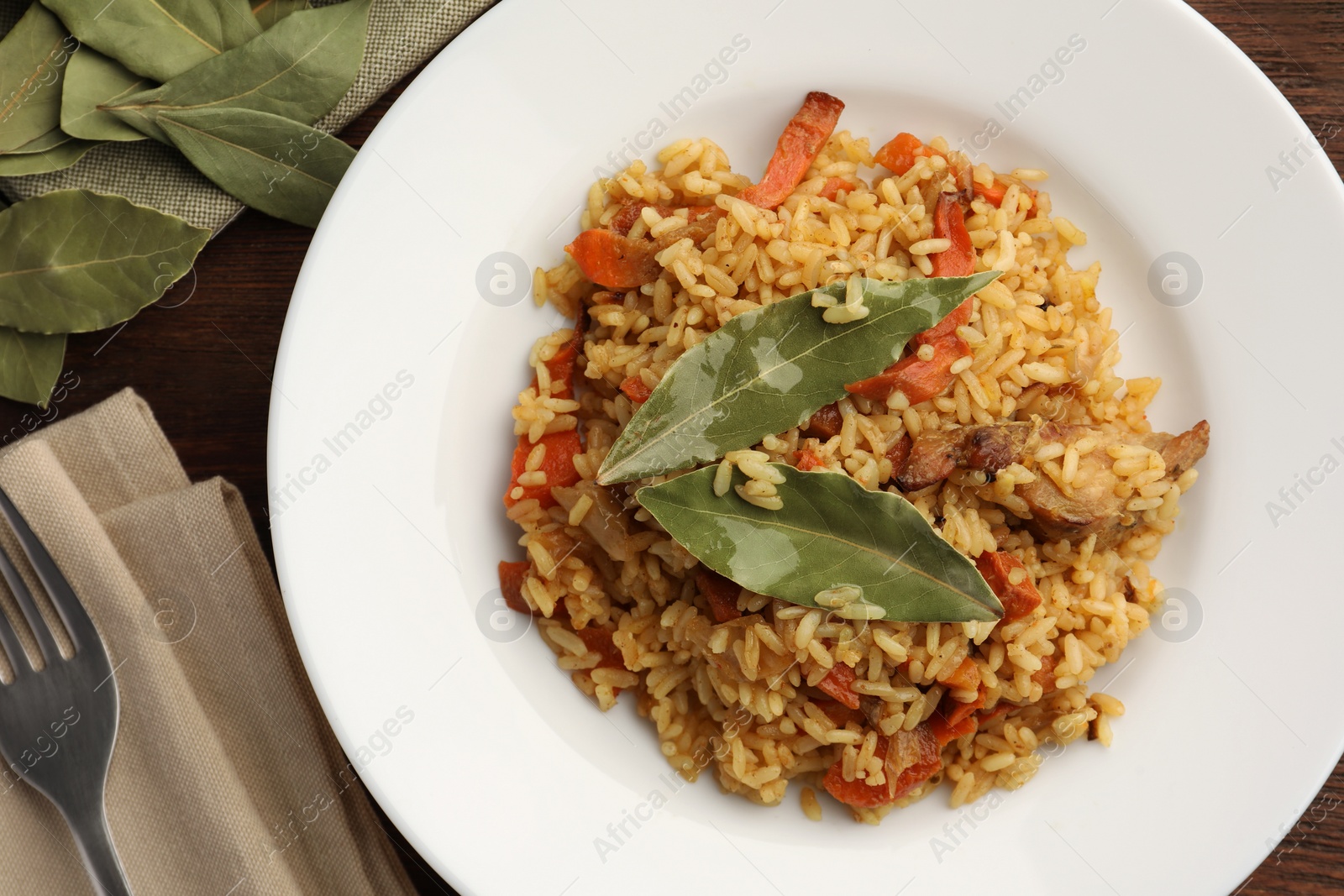 Photo of Delicious pilaf, bay leaves and fork on wooden table, flat lay