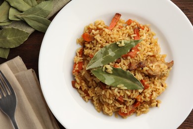 Photo of Delicious pilaf, bay leaves and fork on wooden table, flat lay