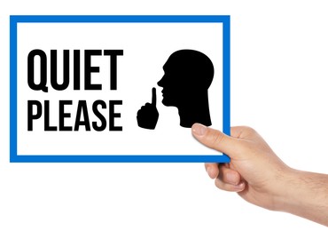Image of Man holding sign with phrase Quiet Please and shush gesture image on white background, closeup